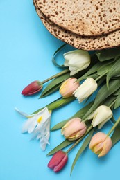 Photo of Tasty matzos and fresh tulips on light blue background, flat lay. Passover (Pesach) celebration