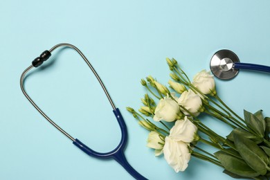 Stethoscope and beautiful eustoma flowers on light blue background, flat lay. Happy Doctor's Day