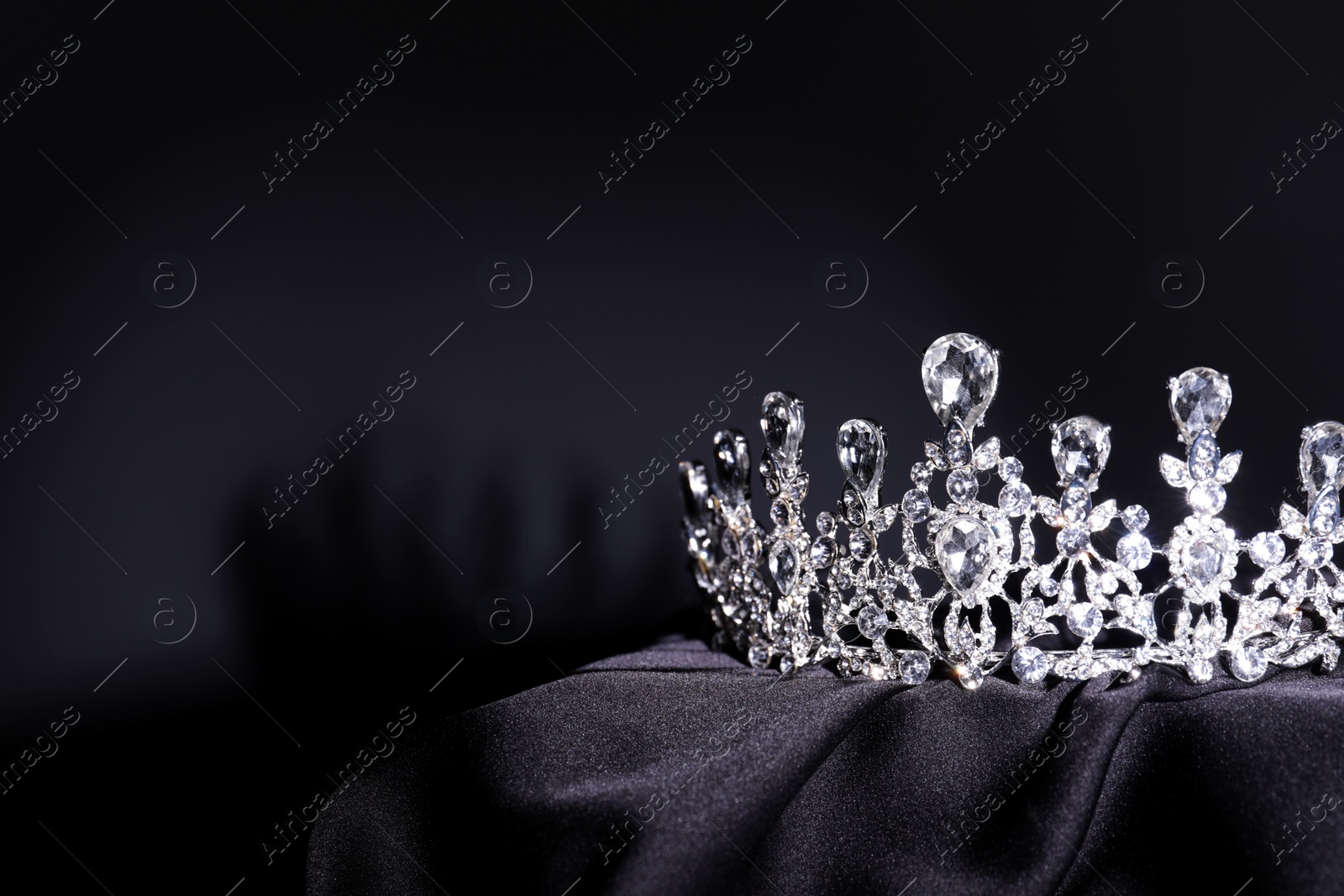 Photo of Beautiful silver tiara with diamonds on black cloth. Space for text