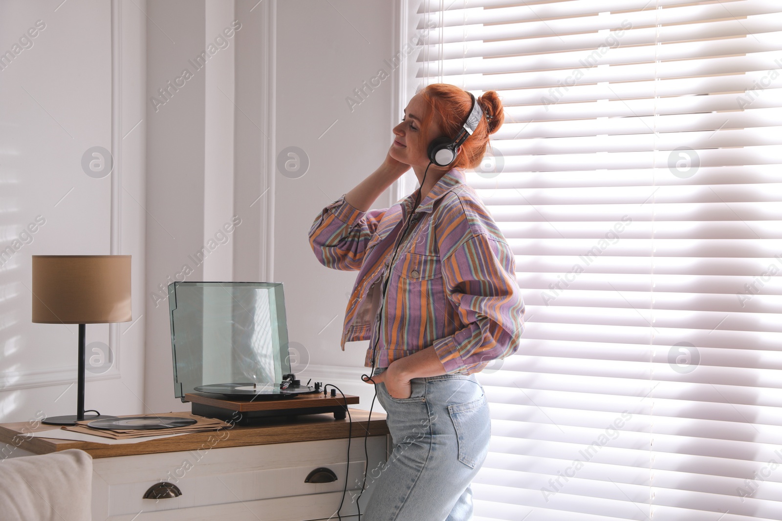 Photo of Young woman listening to music with turntable at home