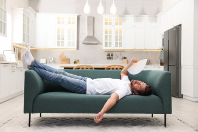 Man waving white hand fan to cool himself on sofa at home