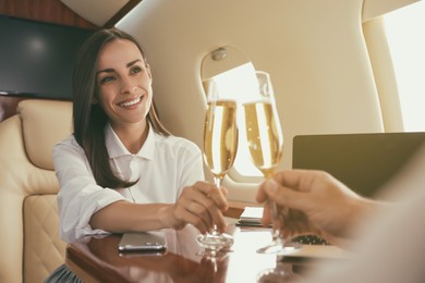 Photo of Colleagues clinking glasses of champagne at table in airplane during flight