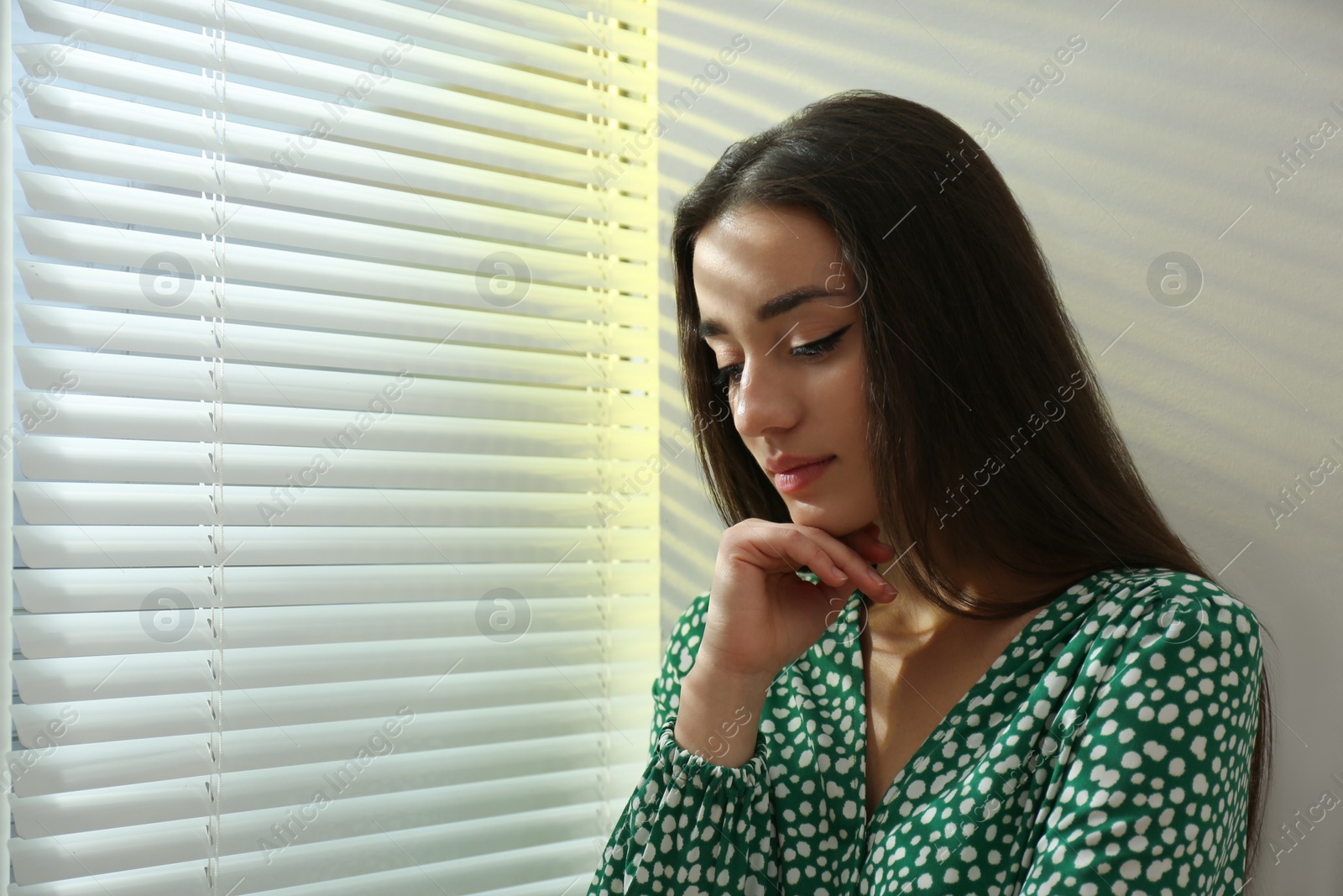 Photo of Young woman near window with Venetian blinds. Space for text