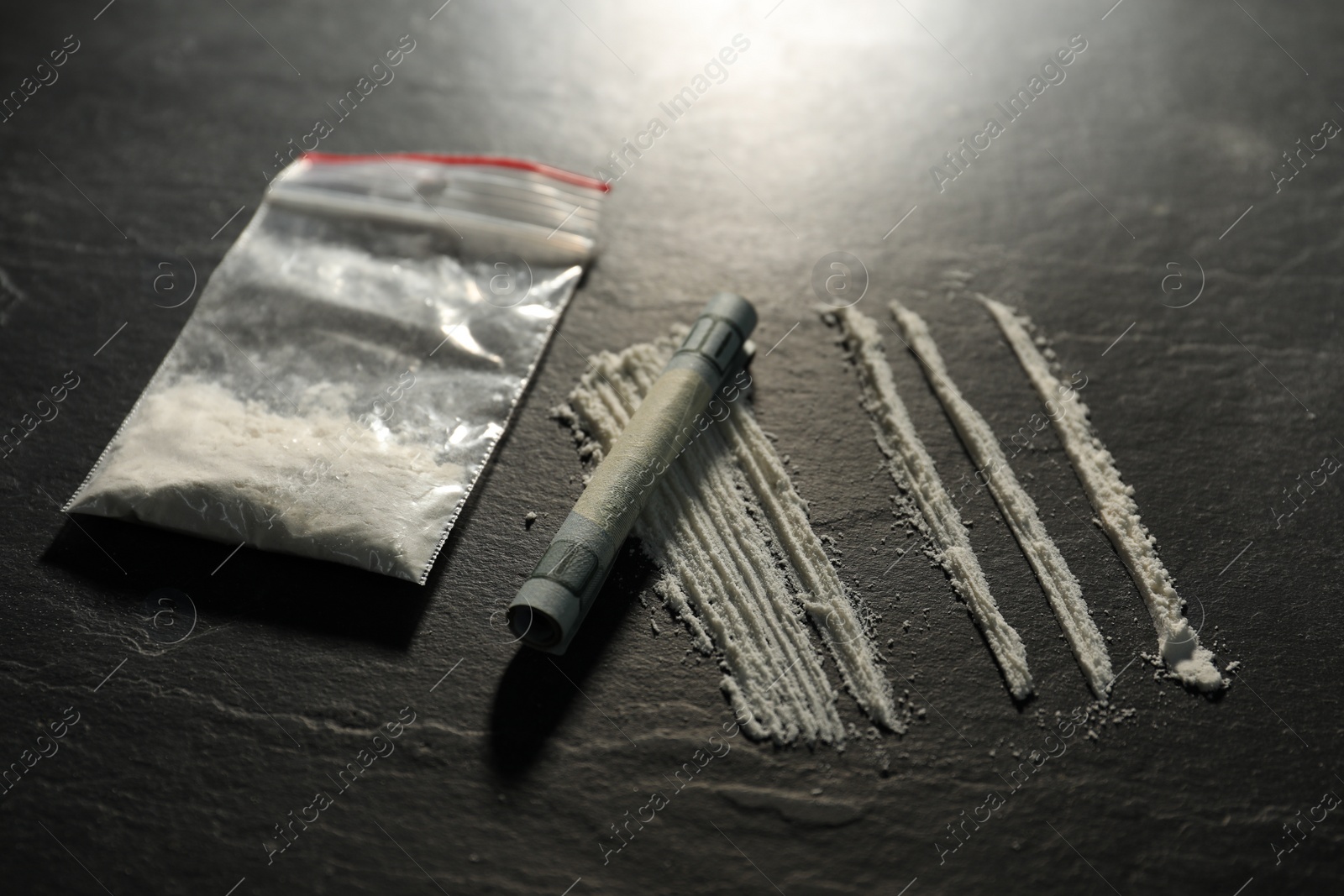 Photo of Drug addiction. Plastic bag with cocaine and rolled dollar banknote on grey textured table, closeup