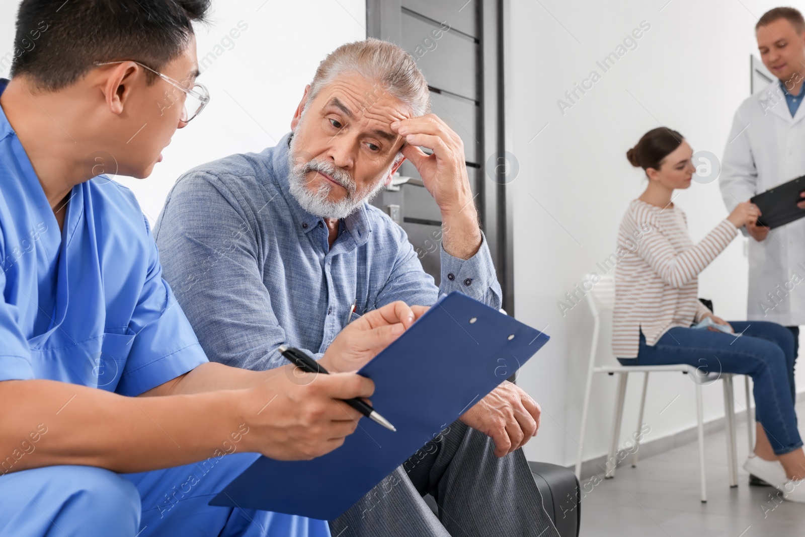 Photo of Doctor with clipboard consulting senior patient in clinic