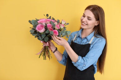 Photo of Female florist holding bouquet of beautiful flowers on color background