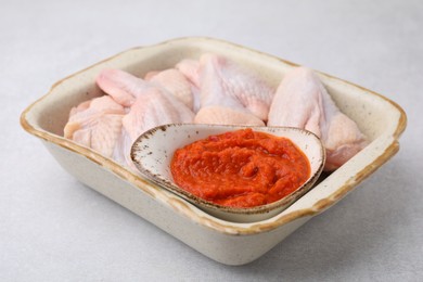 Fresh marinade and raw chicken in baking dish on light table, closeup