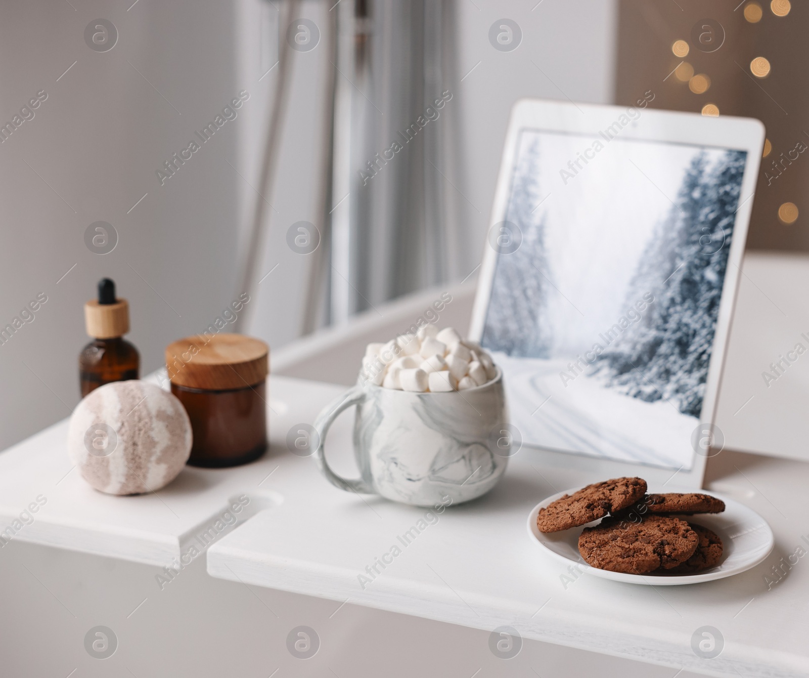 Photo of White wooden tray with tablet, cookies and spa products on bathtub in bathroom