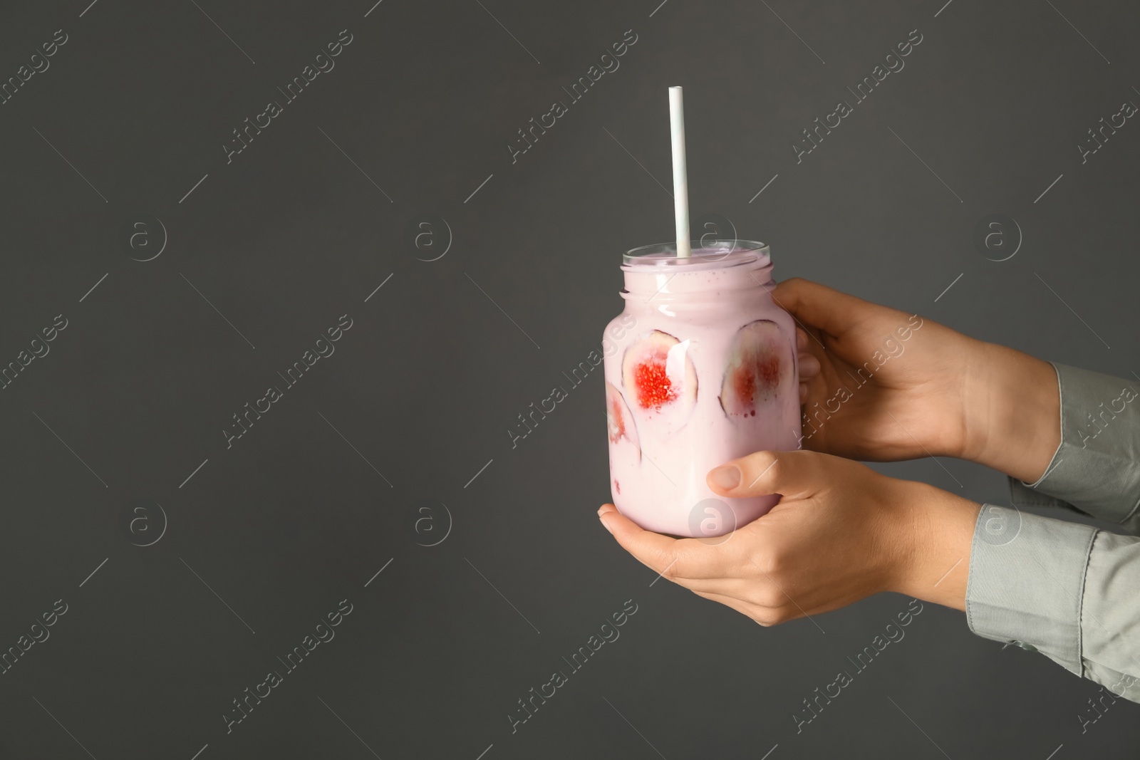 Photo of Woman holding fig smoothie on grey background, closeup. Space for text