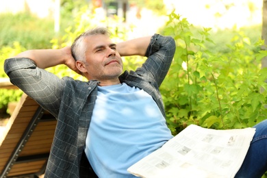 Photo of Handsome mature man with newspaper on bench in park