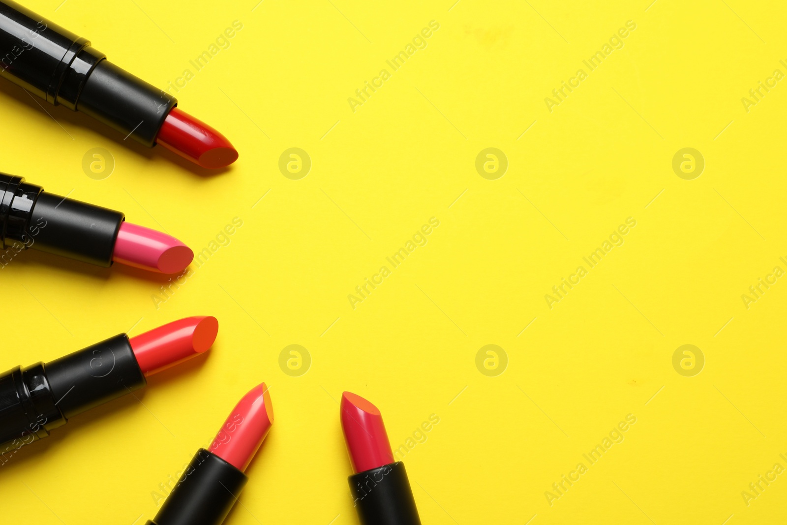 Photo of Many bright lipsticks on yellow background, flat lay. Space for text