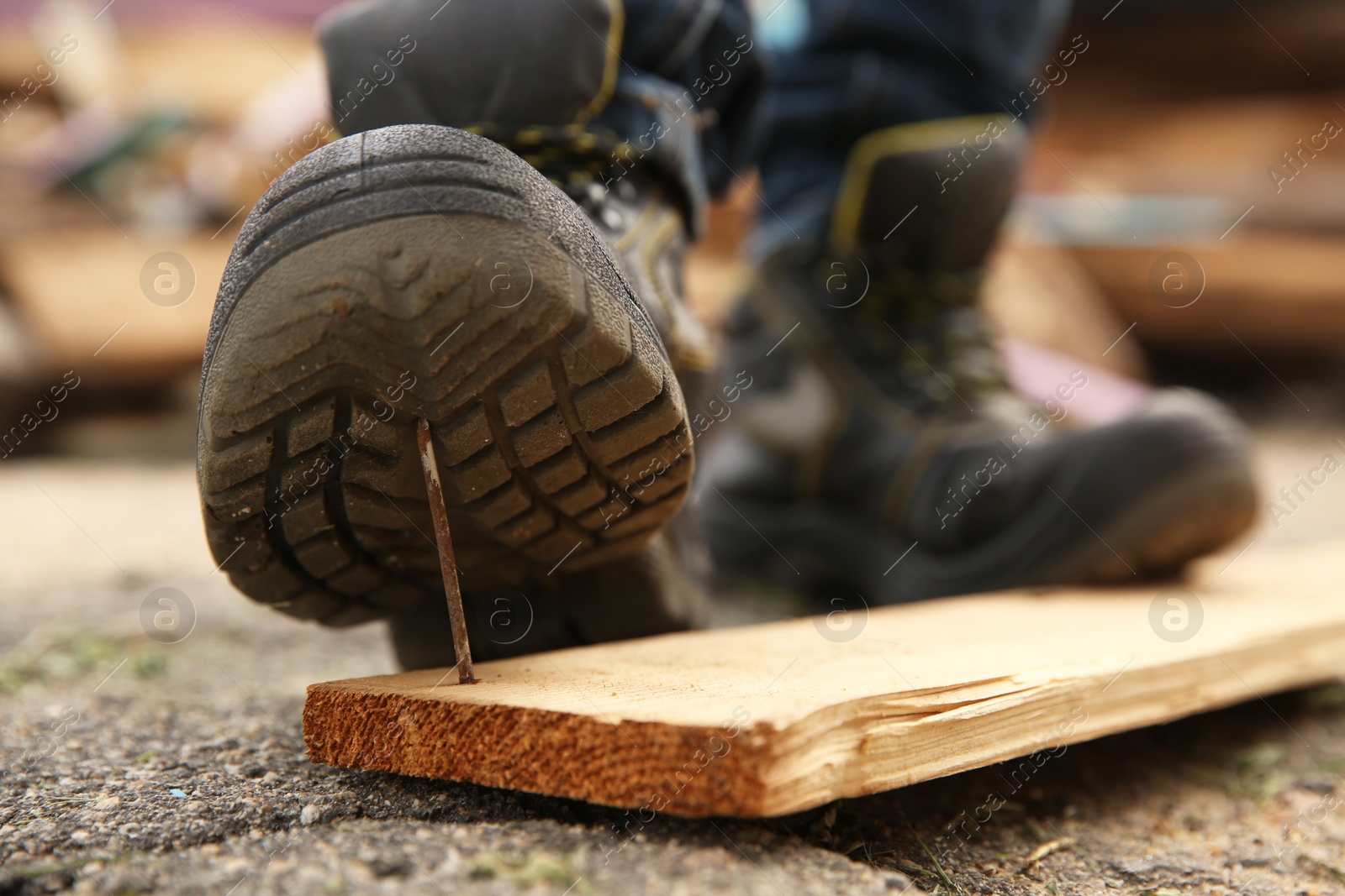 Photo of Careless worker stepping on nail in wooden plank outdoors, closeup