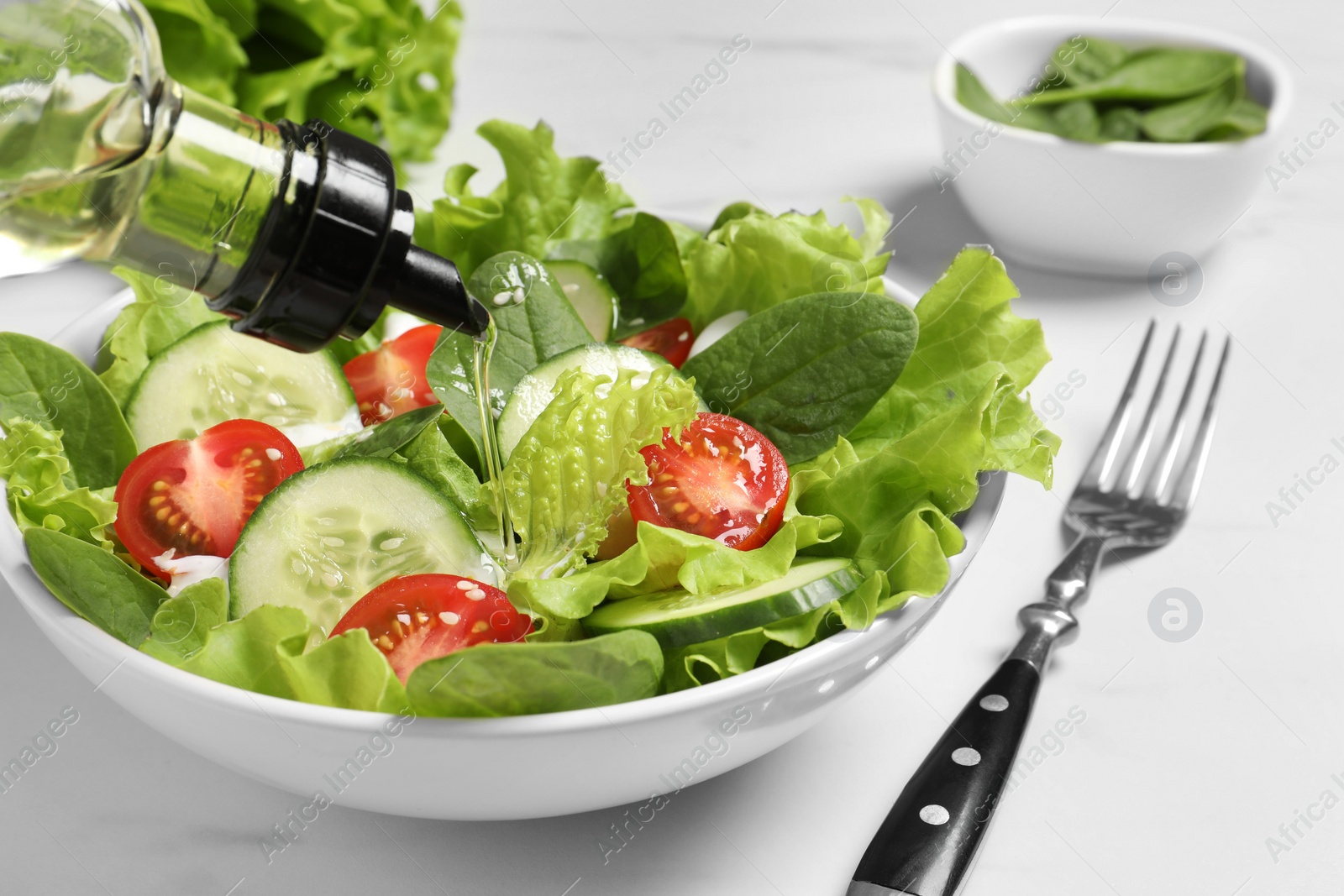 Photo of Pouring oil into delicious salad on white table, closeup