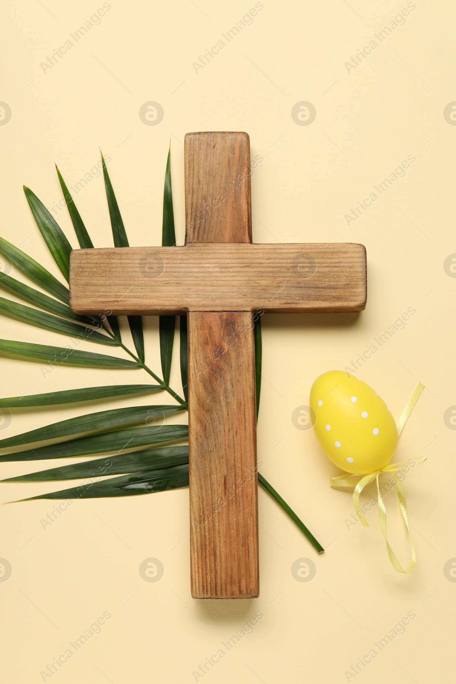 Photo of Wooden cross, painted Easter egg and palm leaf on beige background, top view