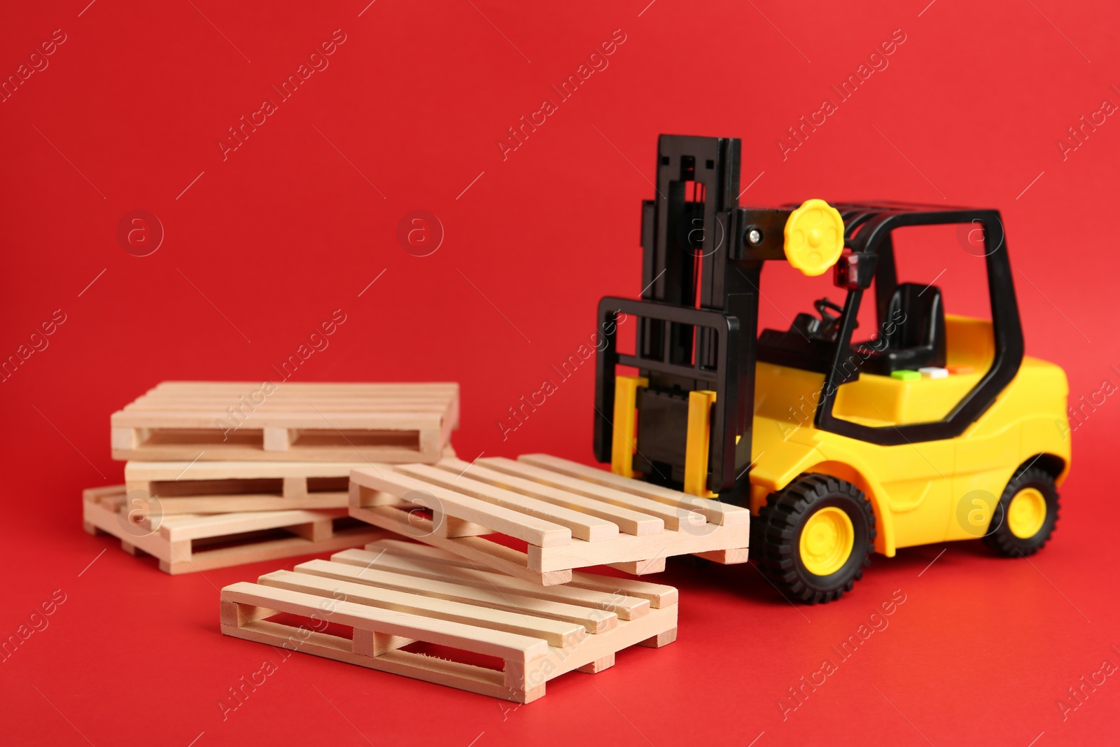 Photo of Toy forklift and wooden pallets on red background