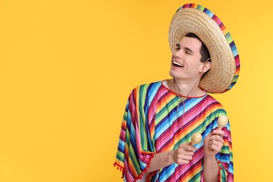 Photo of Young man in Mexican sombrero hat and poncho with maracas on yellow background. Space for text