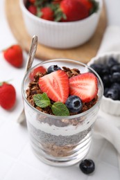 Photo of Tasty granola with berries, yogurt and chia seeds in glass on white table, closeup