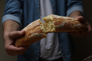 Photo of Man breaking loaf of fresh bread on dark background, closeup