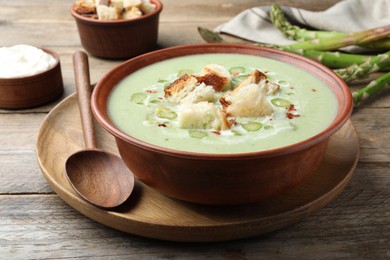 Photo of Delicious asparagus soup with croutons served on wooden table