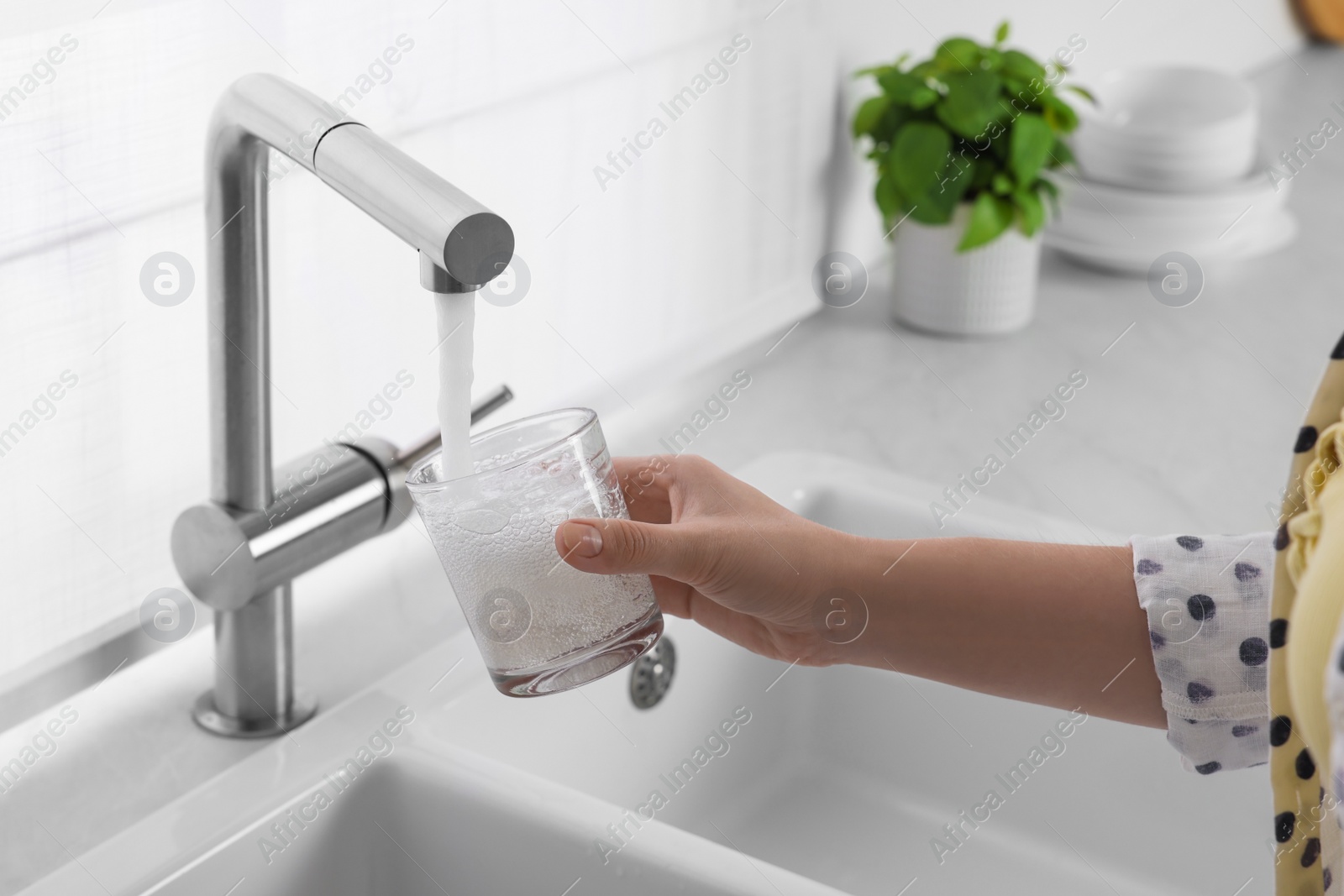 Photo of Woman filling glass with water from tap in kitchen, closeup