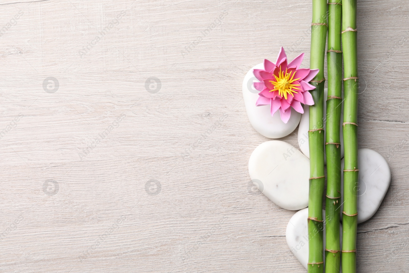 Photo of Spa stones, flower and bamboo stems on light wooden table, flat lay. Space for text