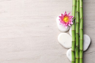 Photo of Spa stones, flower and bamboo stems on light wooden table, flat lay. Space for text