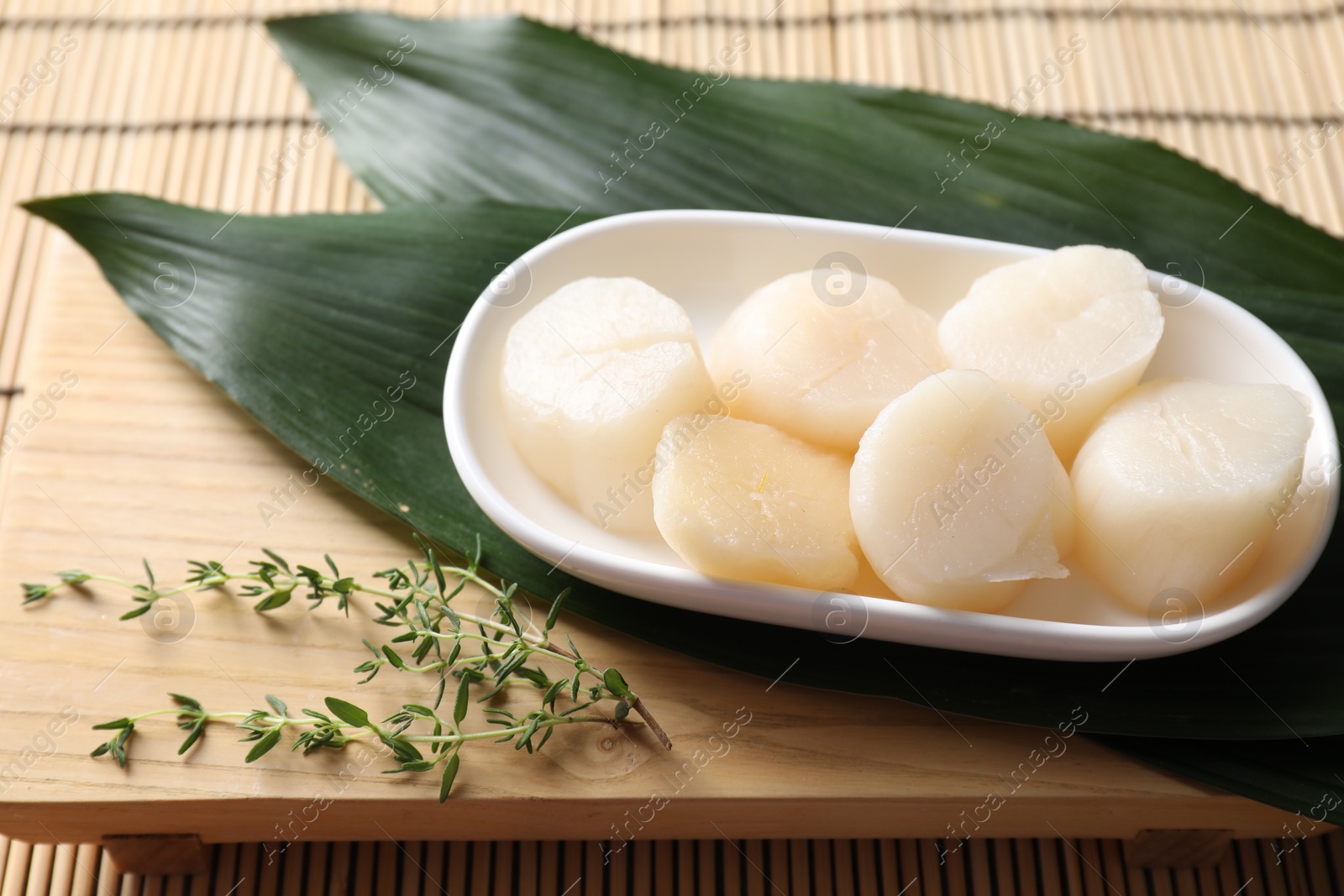 Photo of Fresh raw scallops, thyme and green leaves on bamboo mat