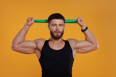 Young man exercising with elastic resistance band on orange background