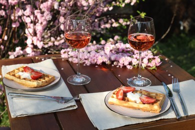 Photo of Delicious Belgian waffles with fresh strawberries and wine served on table in spring garden