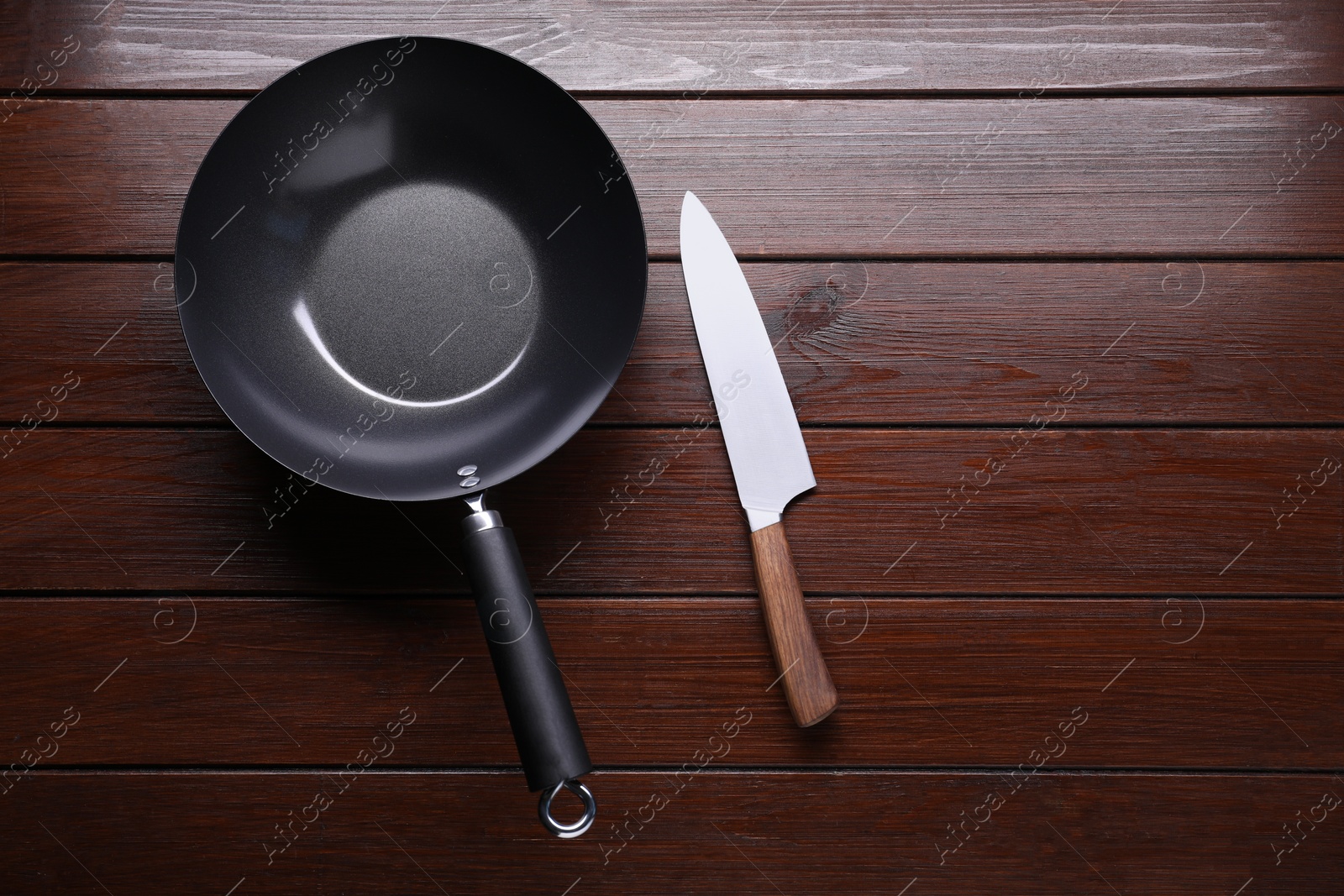 Photo of Empty iron wok and knife on wooden table, flat lay. Space for text