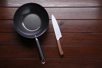 Empty iron wok and knife on wooden table, flat lay. Space for text