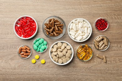 Photo of Different dietary supplements in bowls on wooden table, flat lay