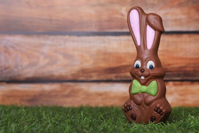 Easter celebration. Funny chocolate bunny on grass against wooden background. Space for text