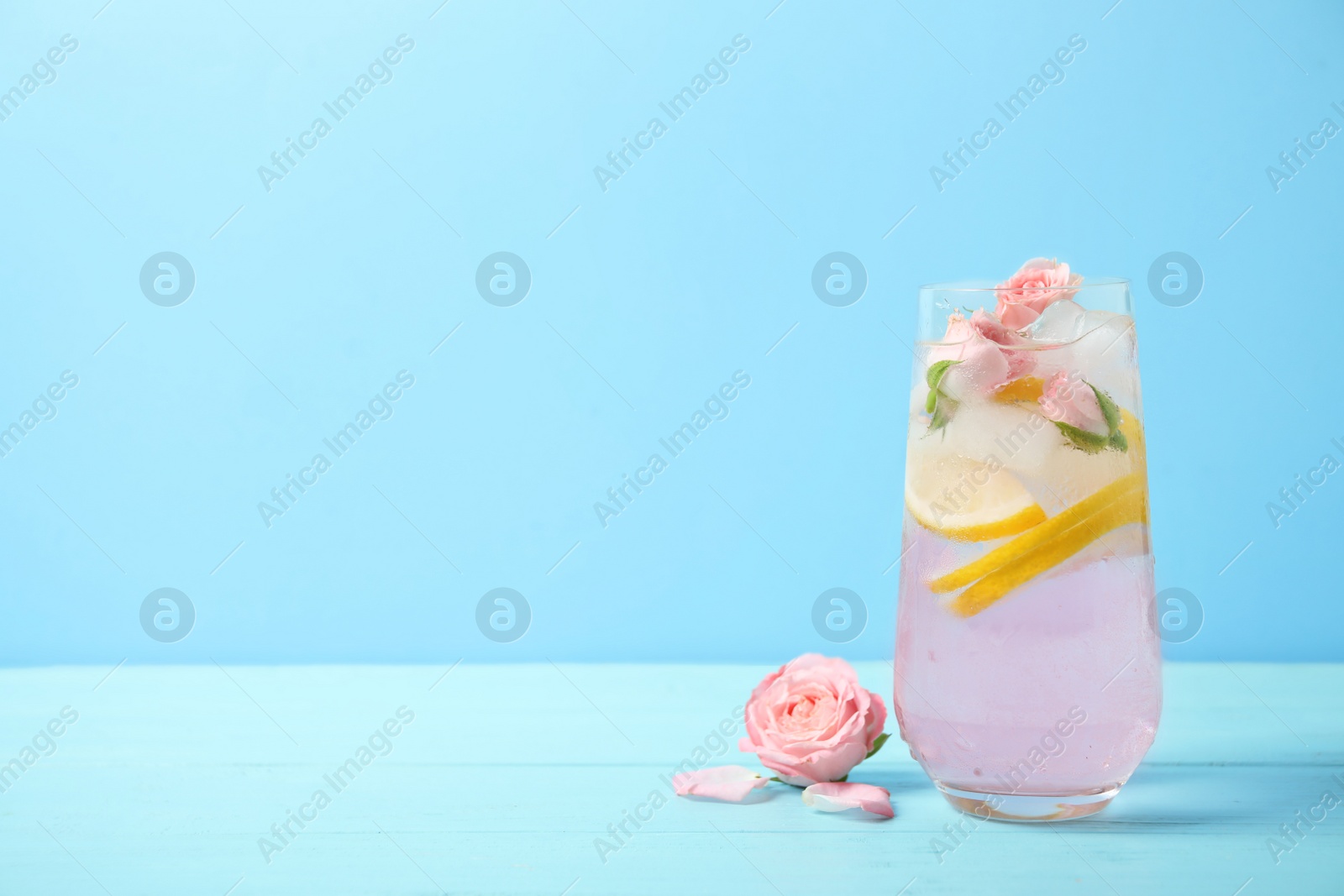 Photo of Tasty refreshing lemon drink with roses on wooden table against light blue background. Space for text