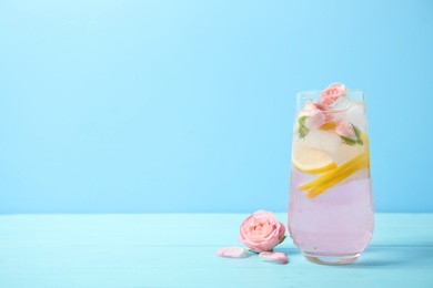 Tasty refreshing lemon drink with roses on wooden table against light blue background. Space for text