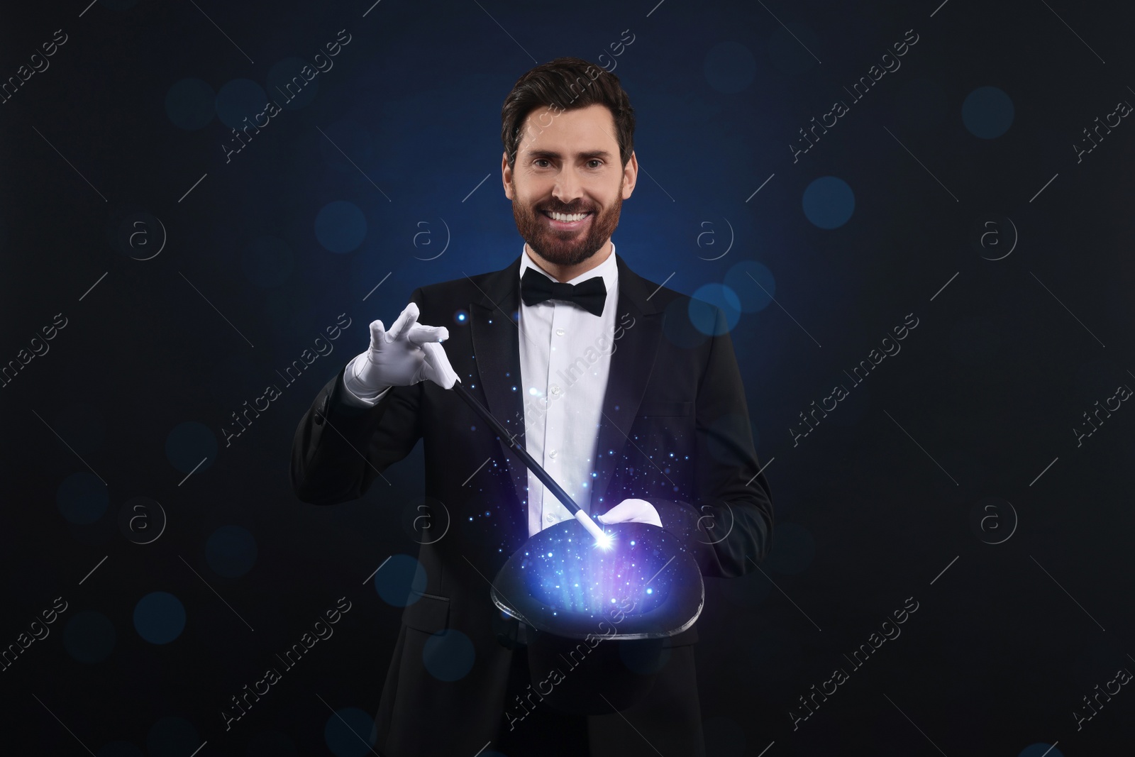 Image of Smiling magician showing trick with top hat and wand on dark blue background