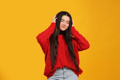 Teenage girl listening music with headphones on yellow background