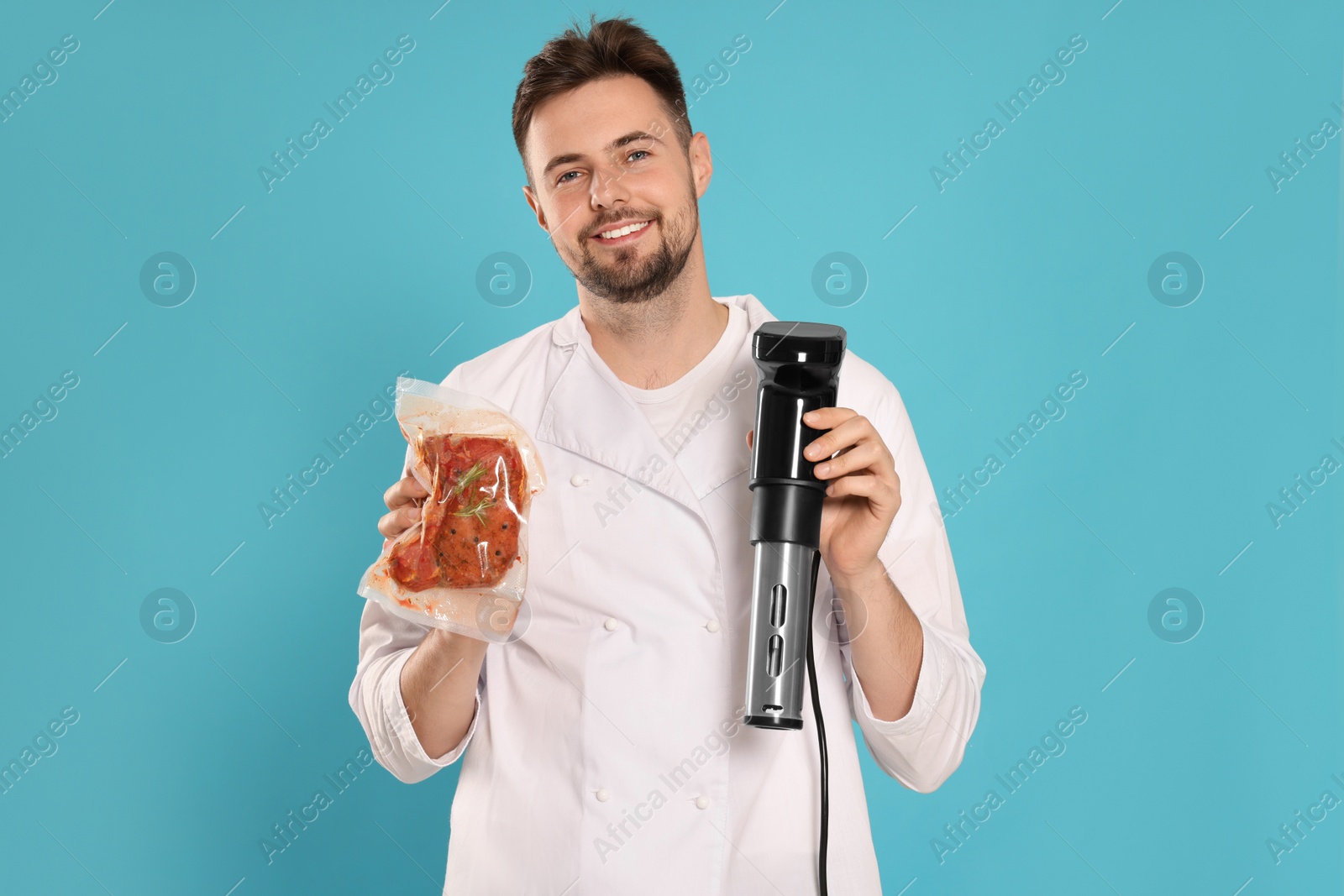 Photo of Smiling chef holding sous vide cooker and meat in vacuum pack on light blue background