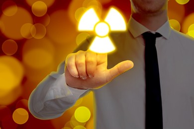 Man touching glowing radiation warning symbol on digital screen against red background with blurred lights, closeup