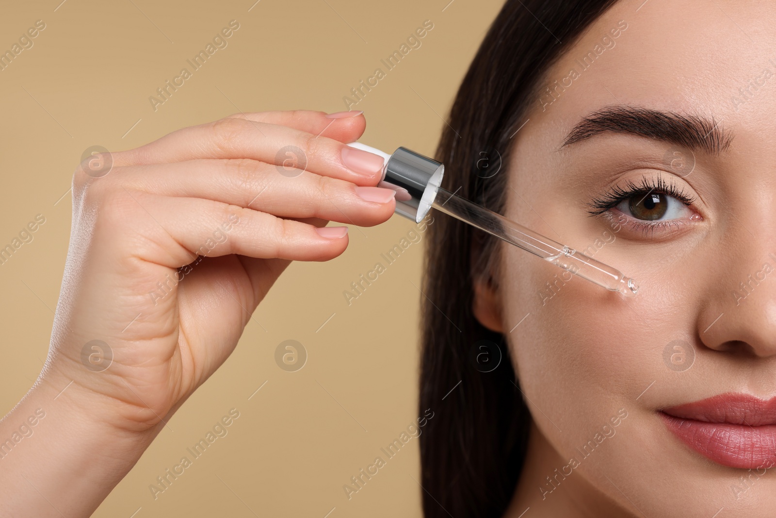 Photo of Young woman applying essential oil onto face on beige background, closeup