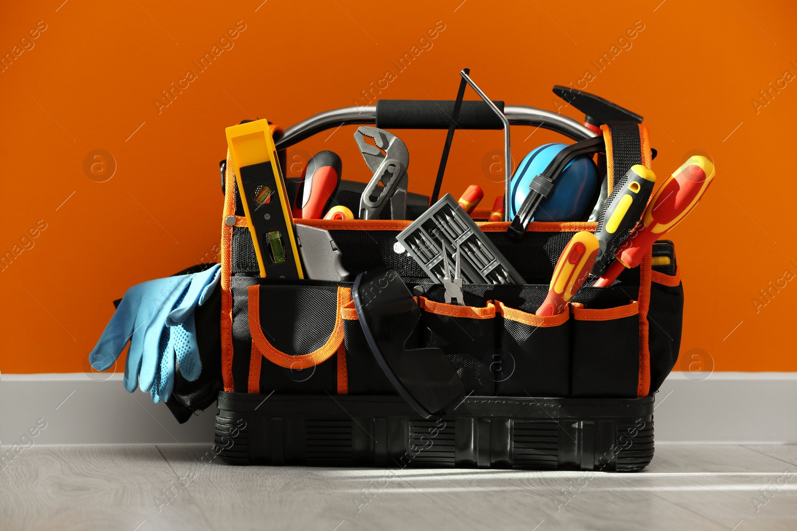 Photo of Bag with different tools for repair on floor near orange wall