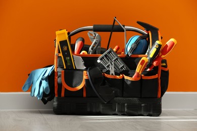 Photo of Bag with different tools for repair on floor near orange wall
