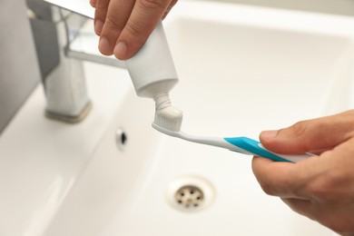 Photo of Man applying toothpaste on brush near sink in bathroom, closeup