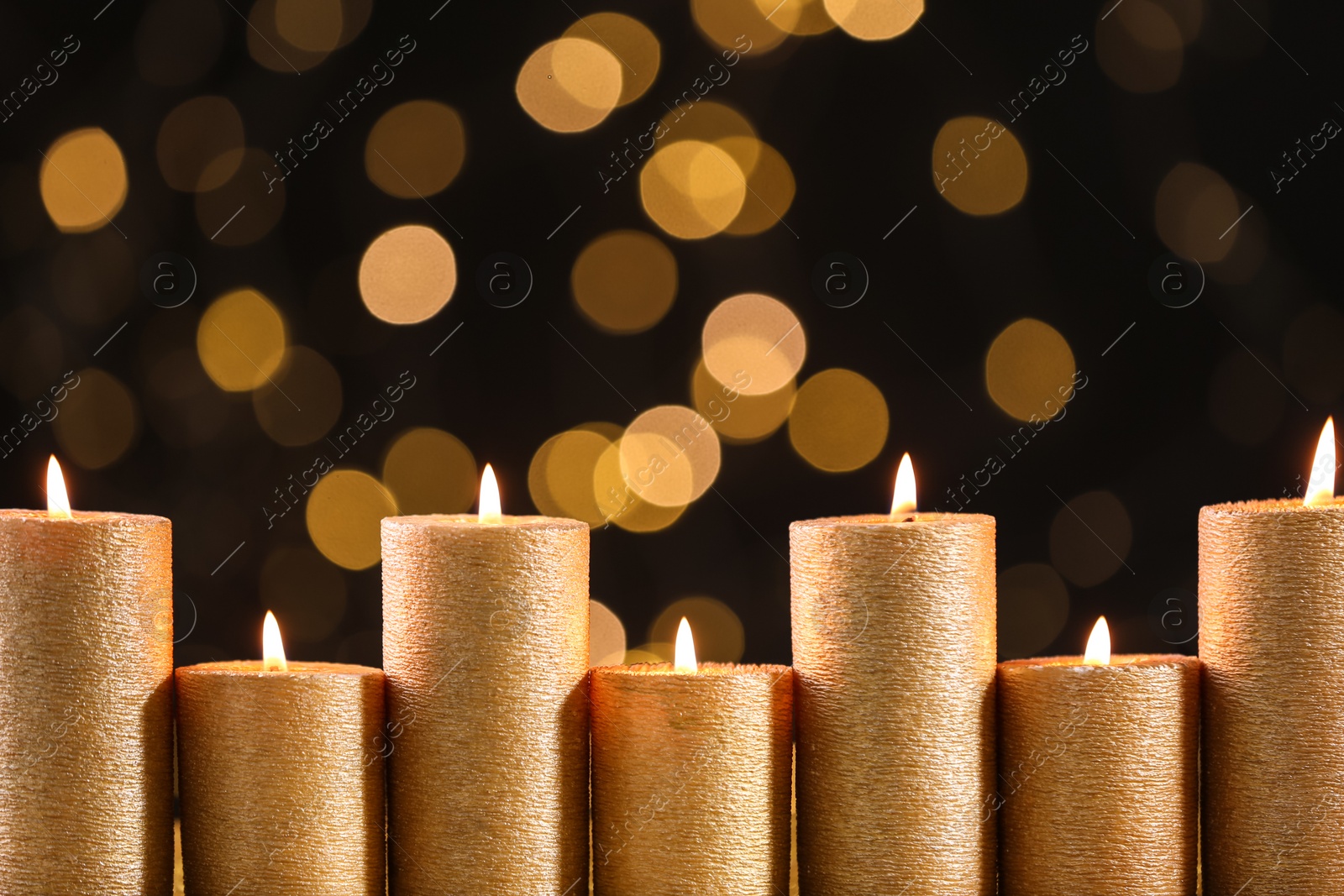 Photo of Golden candles burning against defocused lights. Space for text