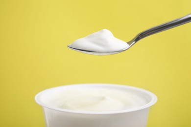Photo of Eating delicious natural yogurt on yellow background, closeup