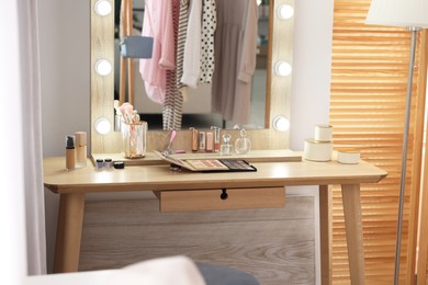 Photo of Makeup room. Stylish mirror with light bulbs and different beauty products on dressing table indoors