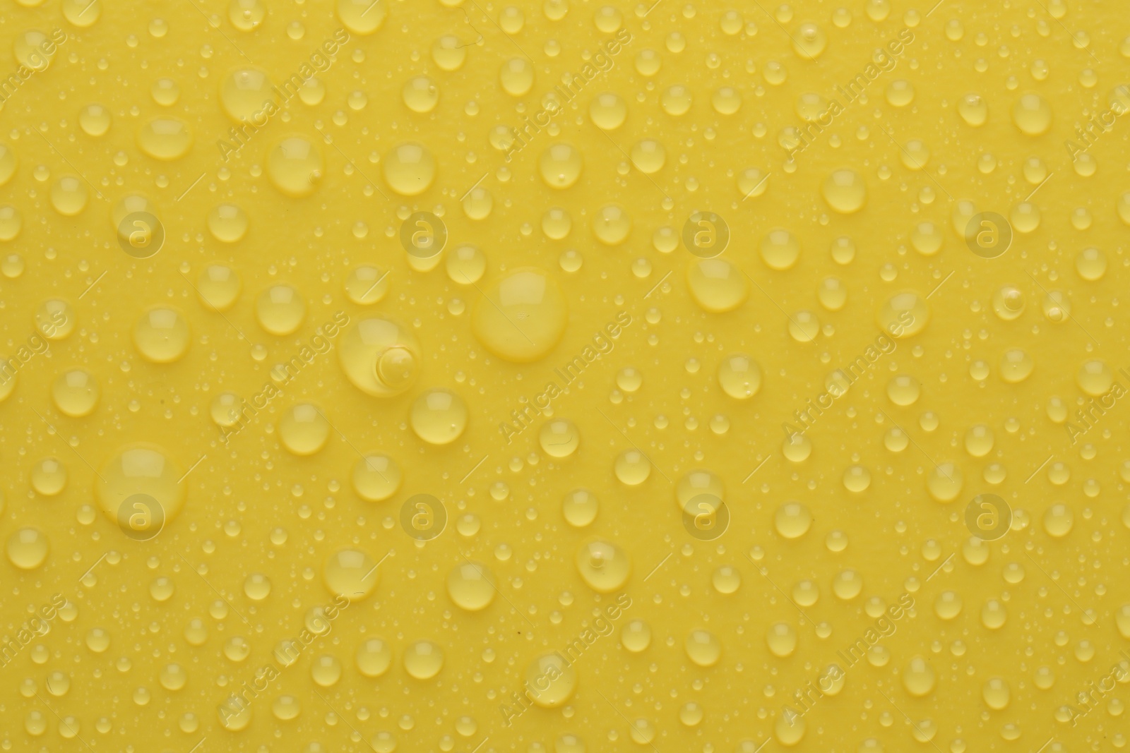 Photo of Water drops on yellow background, top view