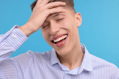 Young man laughing on light blue background