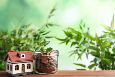 House model and jar with coins on wooden table against blurred background. Space for text