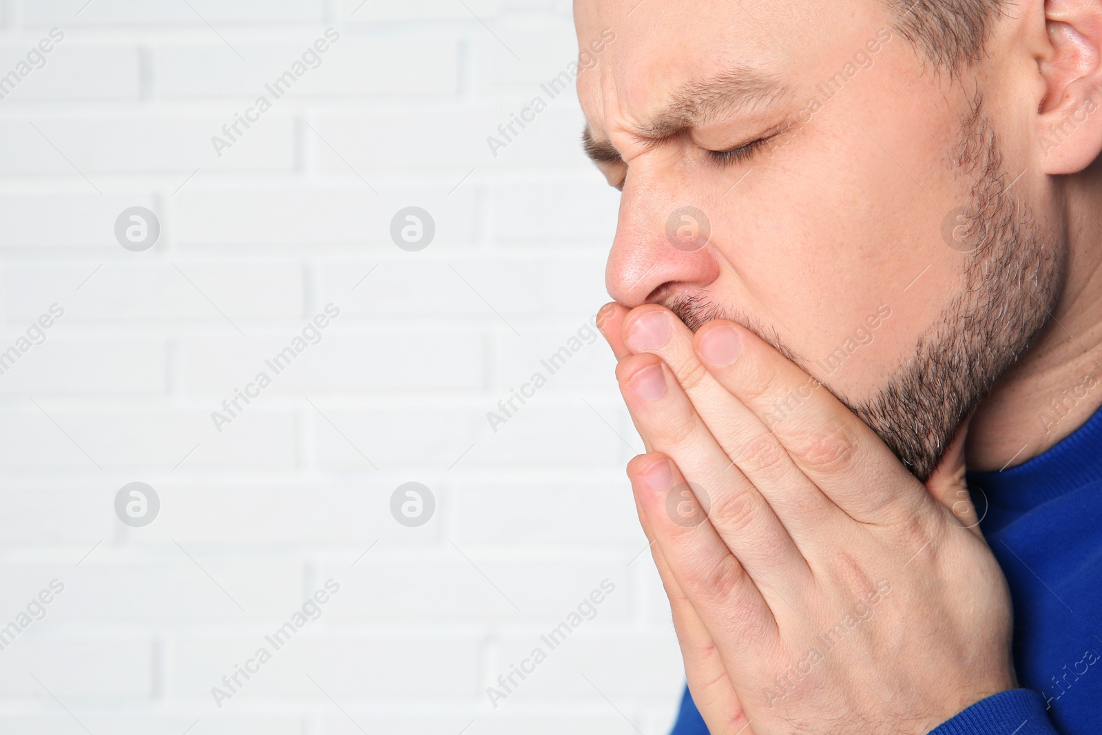 Photo of Man suffering from cough near brick wall. Space for text